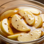 Яблоки в сиропе с ванилью в стеклянной миске на столе — сладкий домашний десерт.